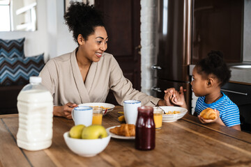 Obraz na płótnie Canvas Black mother and daughter holding hands together while having breakfast