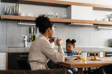 Happy black mother and daughter having breakfast at home kitchen