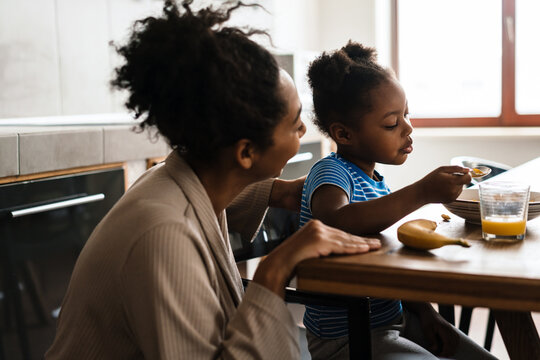 Black Mother And Daughter Having Breakfast At Home Kitchen