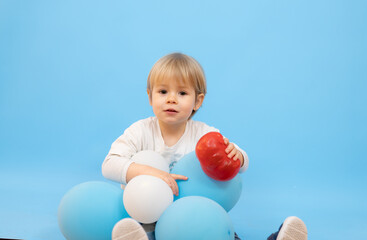 Fototapeta na wymiar Beautiful smiling boy sitting with balloons isolated over blue background.