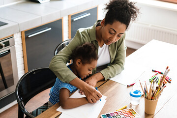Black woman drawing with her happy daughter at home kitchen