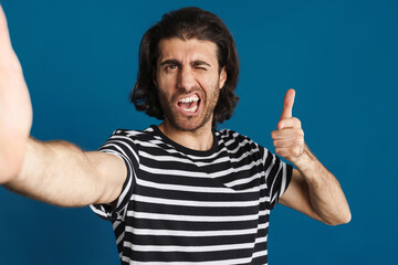 Fototapeta premium Unshaven brunette man pointing finger at camera and taking selfie photo