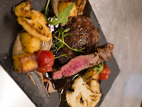 Juicy Beef rump steak from marble beef medium rare with spices and grilled vegetables on black stone plate, close-up.