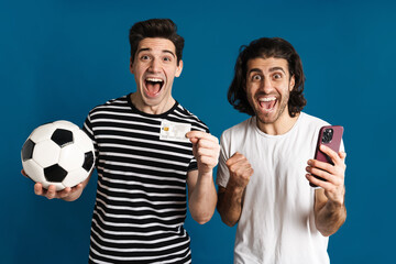 Excited two men using cellphone while holding football and credit card
