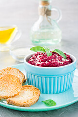 Homemade baked beetroot hummus in a bowl with sesame seeds and basil and baked small toast on a plate on the table. Vertical view