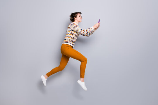 Full length body size profile side view of lovely focused girl jumping running using device isolated over grey pastel color background