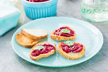 Homemade bruschetta with beetroot hummus on small baked baguette toast on a plate on the table