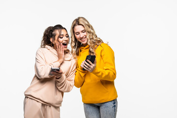 Fototapeta na wymiar Two cheerful young women use smartphones over white background