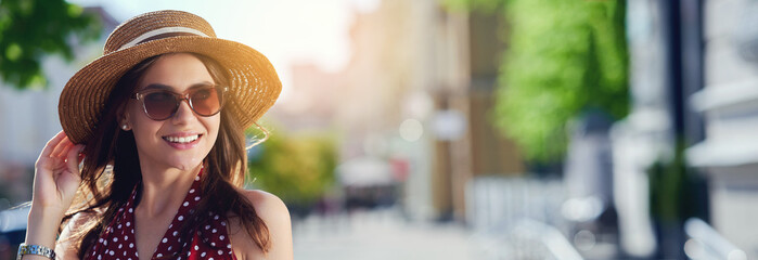 Smiling caucasian woman wearing straw hat sunglasses walking in summer city and enjoying the weather