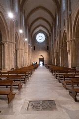 Abbazia medievale con rosone sullo sfondo in alto di 24 colonnine in controluce , in basso una croce bassorilievo , inquadratura verticale con illuminazione artificiale sui pilastri , con archi