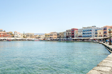 Old Venetian Harbour in Chania, Crete, Greece. Tourists and Locals Walking all Along the Coastline. Beautiful Bay with Multicolored Buildings, Hotels, Taverns and Cafes at the Seafront.