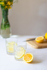 Homemade refreshing summer lemonade drink with lemon slices and ice in glasses with flowers bouquet...