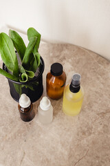 Various amber and matte glass bottles for cosmetics, natural medicine , essential oils or other liquid on a white background standing on a marble podium decorated with a green plant leaves.
