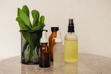 Various amber and matte glass bottles for cosmetics, natural medicine , essential oils or other liquid on a white background standing on a marble podium decorated with a green plant leaves.