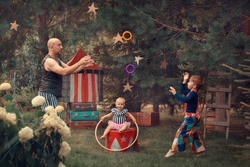Family portrait in vintage circus style. Father is dressed as a strongman with barbell, son is dressed as clown and baby daughter is dressed as pretty assistant. Image with selective focus and toning © Smolina