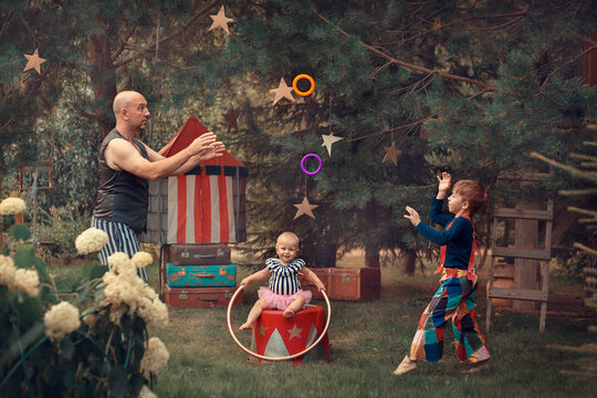 Family portrait in vintage circus style. Father is dressed as a strongman with barbell, son is dressed as clown and baby daughter is dressed as pretty assistant. Image with selective focus and toning