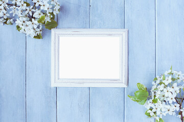 Blank vertical empty picture frame over blue rustic background with spring flowers.