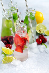 Fototapeta na wymiar Bottles lemonade refreshing summer lemonade with lime, strawberry, cherry, cucumber and ice on a gray concrete background. Mock up.