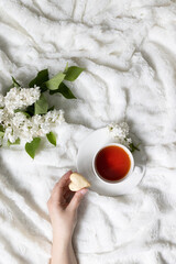Top view of a female hand holding love cookies. Cup of fragrant herbal tea on a white bed frame