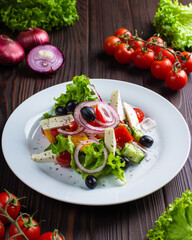 Vegetable salad with cheese and olives in a white plate on a wooden table. Restaurant, menu, recipe. Close-up, front view 