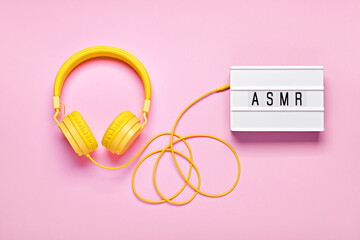 Yellow headphones and ASMR letters lightbox on pink background. ASMR Stress-relieving sounds concept, flat lay