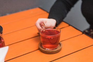 Cup and teapot with fruit tea held by female hands on the table in a coffee shop
