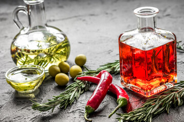 Bottles with chili and olive oils and herbs on stone background