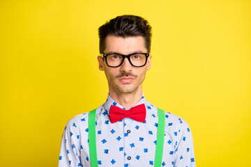 Portrait of attractive calm serious guy wearing specs print shirt isolated over bright yellow color...