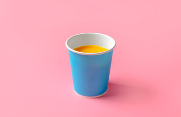 Orange juice in a disposable paper cup, against a pink background. Disposable tableware. High quality photo