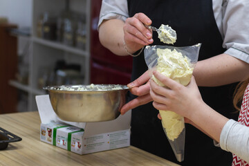 The chef fills a pastry bag with buttercream for filling eclair cakes
