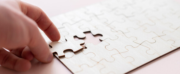 hand holding a jigsaw piece and complete puzzle on the table