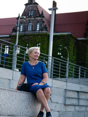 Happy elderly blonde woman in blue dress in summer park.