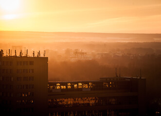 a bright orange sunset lights up buildings, an industrial area, and a river covered in snow