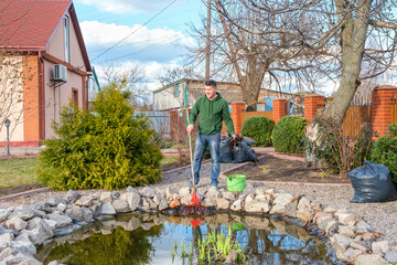 Mature caucasian man cleans a garden pond from water plants and falling leaves. Spring seasonal pond care after winter.