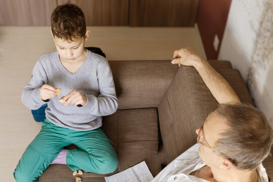 A Portrait Of Boy With Wooden Puzzle In The Hand And A 65 Year Old Smiling Man On Light Background. Human Interaction Grandfather And Grandson, Together Activities.