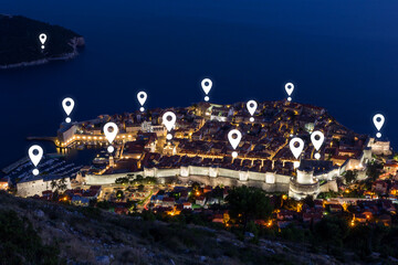 Fototapeta premium Map pin icons on Dubrovnik's cityscape at dusk. Walled Old Town of Dubrovnik in Croatia viewed from above at night.