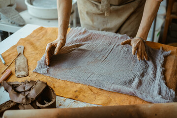 A woman in an apron works with her hands with clay. On the table clay, rolling pin and a piece of...