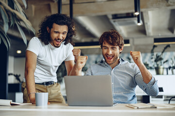 Two excited overjoyed young businessmen looking at laptop screen happy to win or recieved good news