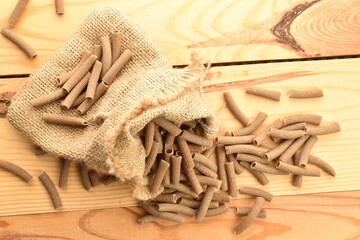 Dark brown, uncooked, organic rye pasta with a jute bag on a wooden table, close-up, top view.