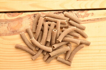 Dark brown, not cooked, organic rye pasta on a wooden table, close-up, top view.