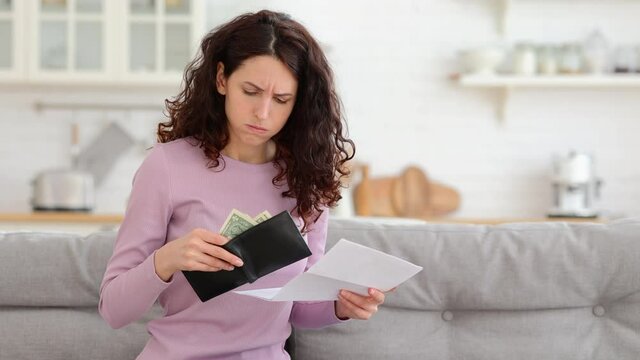No money left. Unhappy sad girl holding last cash money in wallet, papers calculate domestic bills at home. Millennial woman frustrated about lack of finances, feeling anxiety about debt or bankruptcy