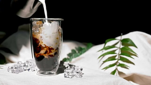 Barista pouring milk into a glass of iced coffee