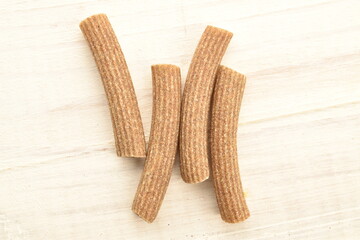 Dark brown, not cooked, organic rye pasta on a wooden table, close-up, top view.