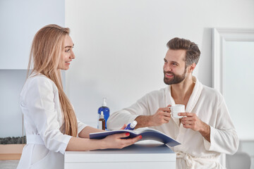 Medical worker consults with brochure and beauty treatments to patient. Patient young man standing near the reception and holding tea