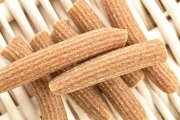 Dark brown, uncooked, organic rye pasta on a vine mat, close-up, top view.