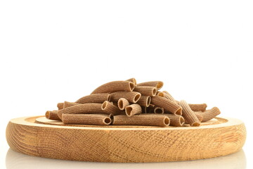 Dark brown, uncooked, organic rye pasta on a wooden tray, close-up, isolated on white.