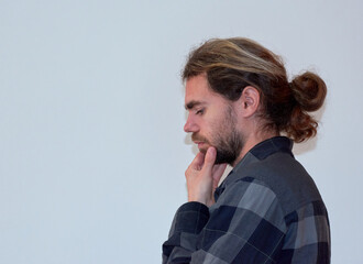 A side view of a Spanish young bearded male thinking with his hand on his chin on the white background