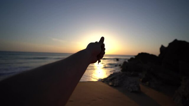 Mano a contraluz soltando arena con el sol de fondo