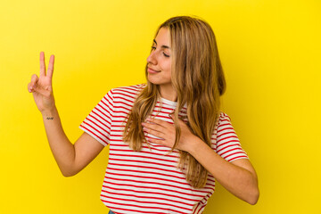 Young blonde caucasian woman isolated on yellow background taking an oath, putting hand on chest.