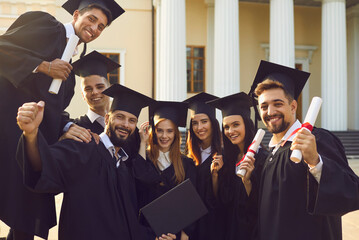 Group portrait of happy graduates near their alma mater. Smiling university students in traditional...